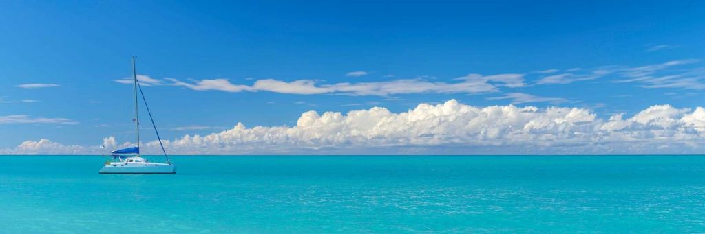 Panoramic view of a blue seascape with sailboat and cloudy sky