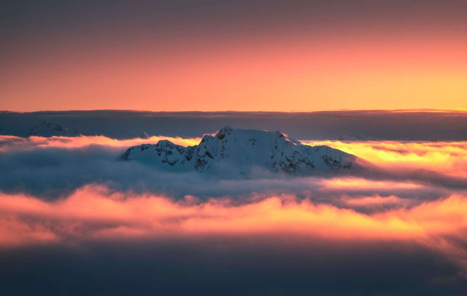 Besneeuwde bergtop in wolkenzee