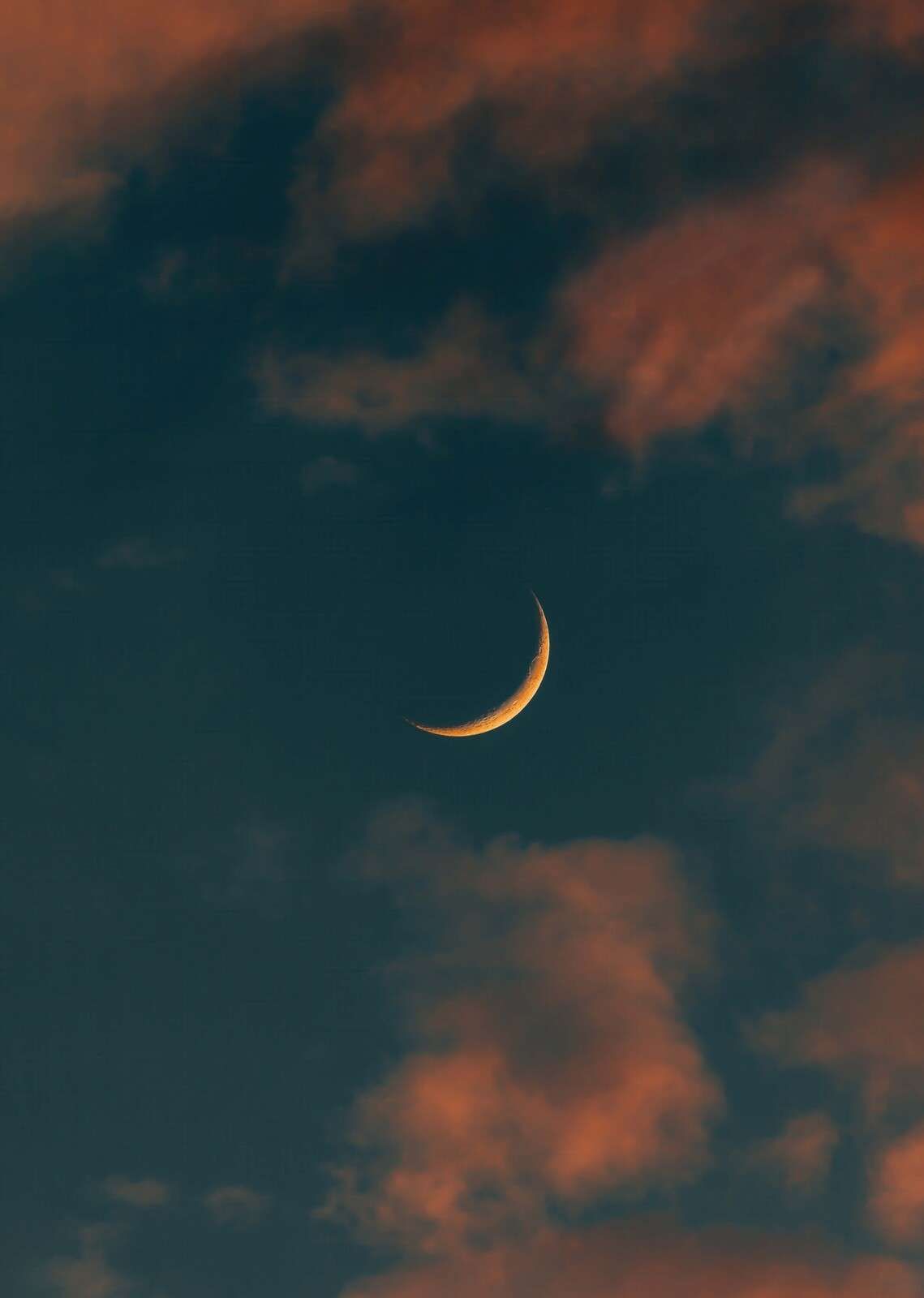 Smalle maan tussen vurige wolken